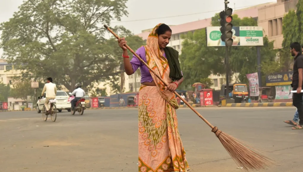 A woman sweeping the street in India, diligently cleaning the public space with a broom.